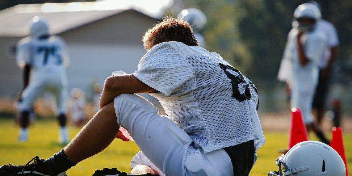 selective focus photography of man sitting on field wearing football gear